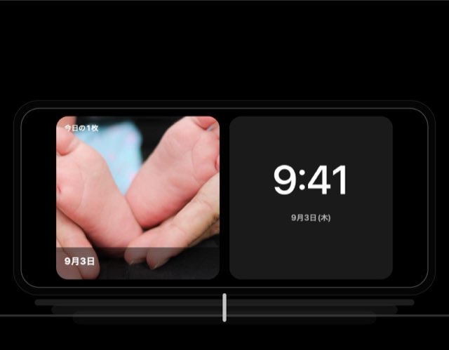 An iPhone lying sideways on a charger, showing today's photo next to the clock in StandBy